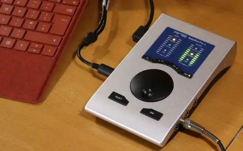 Srebrny interfejs audio RME Babyface Pro FS podłączony do czerwonej klawiatury. Idealny do mobilnego studia.