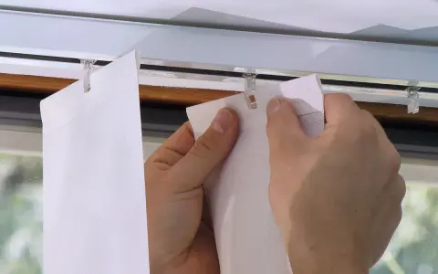 Hände befestigen einen Lamellenvorhang in einer Gardinenschiene mit Clips.