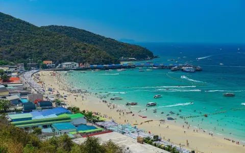 Ein belebter Pattaya Strand mit vielen Menschen, Sonnenschirmen und Booten im türkisfarbenen Meer.