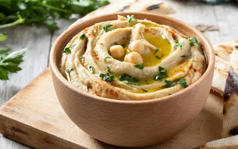 Hummus cremoso en cuenco de madera, decorado con garbanzos, aceite de oliva y perejil. Perfecto para aprender como hacer hummus casero.