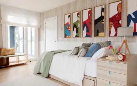 Habitación adolescente chico con cuadros de superhéroes, cama blanca con mantas verdes y cojines, mesita de noche de madera y ventana grande.