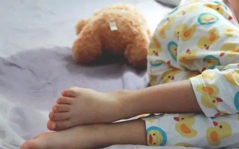 Ein Kind schläft im Pyjama mit Entenmuster, ein Teddybär liegt daneben. Es ist ein friedlicher Moment, in dem das Kind nachts ein und merkt es nicht.