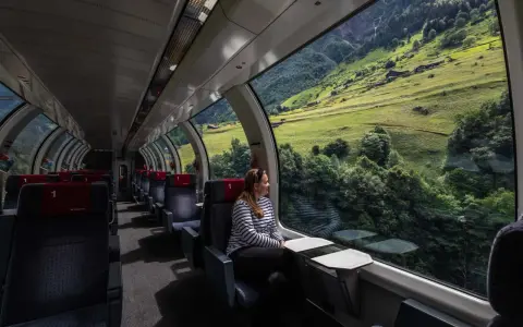 Kobieta w pociągu z panoramicznym widokiem na zielone szwajcarskie góry.
