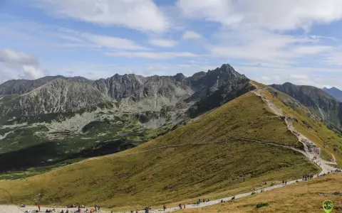 Szlak na Kasprowy Wierch jest popularny, turyści wędrują kamienistą ścieżką pośród zielonych zboczy Tatr.