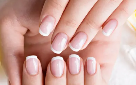 Dłonie z idealnym french manicure, gdzie białe końcówki paznokci lśnią jak tytanowe paznokcie.