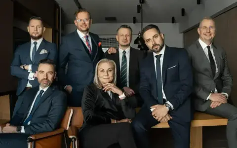 Grupa profesjonalistów w garniturach pozuje do zdjęcia w nowoczesnym biurze.