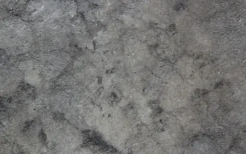 Textura rugosa y desigual de hormigón gris, con zonas más oscuras que sugieren desgaste o humedad.