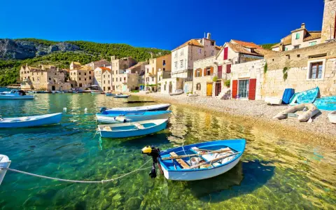 Barchette azzurre in un mare cristallino, un invito a scoprire dove andare al mare in Croazia. Case di pietra e colline verdi fanno da sfondo.