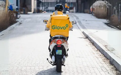 Kurier Glovo na skuterze, w żółtej kurtce z logo, przemierza ulicę. Zastanawiasz się, ile zarabia pracownik Glovo?