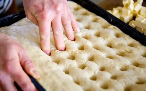 Hände drücken Vertiefungen in den Teig für ein Butterkuchen Rezept. Würfel aus Butter liegen bereit.