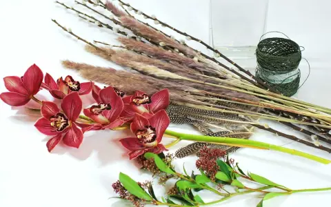 Ciemnoróżowe orchidee, trawy, pióra i gałązki tworzą kompozycję zrównoważoną.