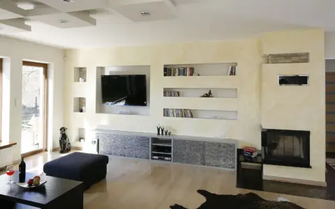 Nowoczesna zabudowa pod telewizor z karton gipsu, z wnękami na książki i dekoracje.