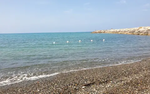 Spiagge più belle della Marina di Cecina: mare azzurro, ciottoli levigati e un molo roccioso con qualche bagnante.
