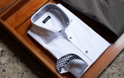 Camicia bianca piegata, con colletto e polsini a quadri marroni e neri, che mostra diversi tipi di polsini camicia.
