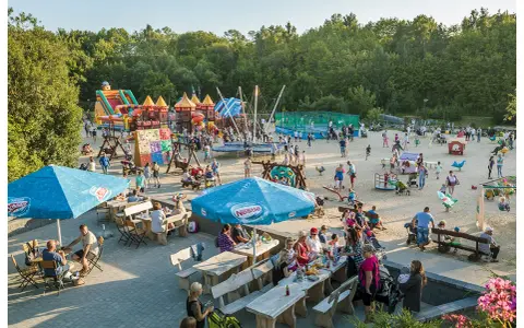 Rodzinna zabawa na placu zabaw w Ocean Park Władysławowo. Dzieci szaleją na dmuchanych zamkach, trampolinach i zjeżdżalniach, podczas gdy dorośli odpoczywają przy stolikach.
