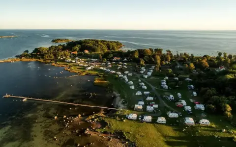 Vacker vy över Kronobergs camping med husvagnar och husbilar utspridda bland träd och vid vattnet. En brygga sträcker sig ut i det klara vattnet.