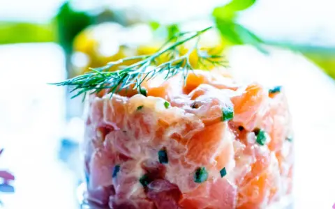 Tartare di salmone fresco, finemente tagliato e condito, guarnito con aneto. Un piatto leggero e saporito.