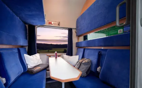 Gemütliche Kabine im Holland Zug mit blauen Sitzen, einem Tisch und Blick auf die Landschaft bei Sonnenuntergang.