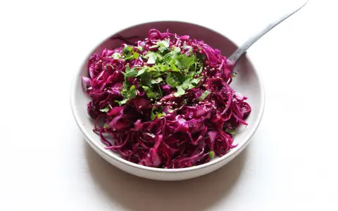 Salade colorée de chou rouge râpé, garnie de coriandre fraîche et de graines de sésame. Une idée simple pour une recette chou rouge savoureuse.