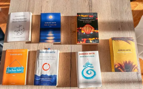 Una collezione di **libri** di Gianluca Gotto disposti su un tavolo di legno. Tra i titoli: "Le coordinate della felicità", "Come una notte a Bali", "La Pura Vida".