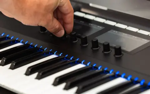 Main d'un musicien ajustant un bouton sur un clavier de musique numérique, avec des touches illuminées de bleu.