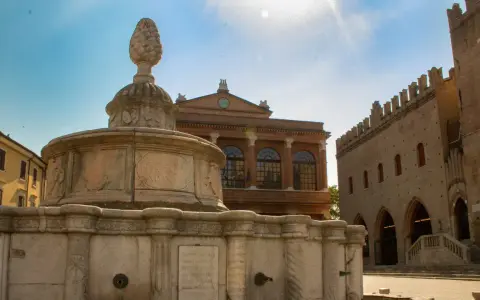 Fontana in pietra con pigna, edifici storici e cielo azzurro. Un assaggio dei monumenti di Rimini.