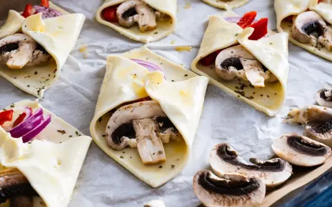 Gotowe do pieczenia przekąski z ciasta francuskiego z pieczarkami, papryką i cebulą.