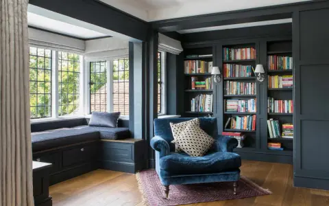 Acogedor rincón lectura salón con sillón azul, ventana con banco y estanterías llenas de libros.