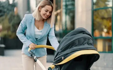Uśmiechnięta kobieta w eleganckim stroju, z wózkiem dziecięcym, symbolizuje powrót do pracy po macierzyńskim.