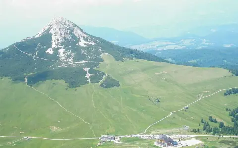 Panoramica delle malghe al Passo Lavazè, con un imponente monte sullo sfondo e sentieri che si snodano tra prati verdi.