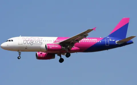 Samolot Wizz Air z różowo-fioletowym ogonem leci na tle błękitnego nieba. Sprawdź wizz discount club cena i leć taniej!