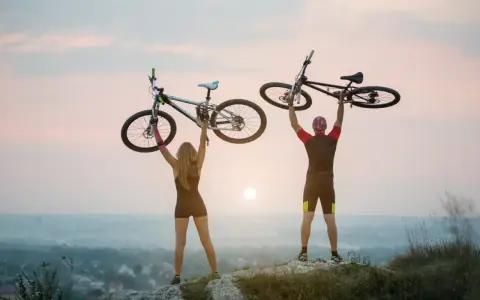 Para rowerzystów świętuje na szczycie, unosząc rowery. To idealny moment na odkrywanie najpiękniejsze odcinki z green velo.