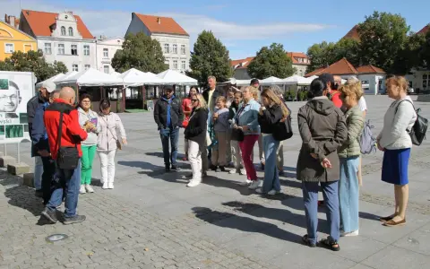Grupa turystów słucha przewodnika na rynku w Chełmnie, poznając lokalną trasę.