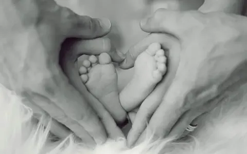 Manos de padre formando un corazón alrededor de los pies de su bebé, un símbolo de apego excesivo al padre y amor incondicional.