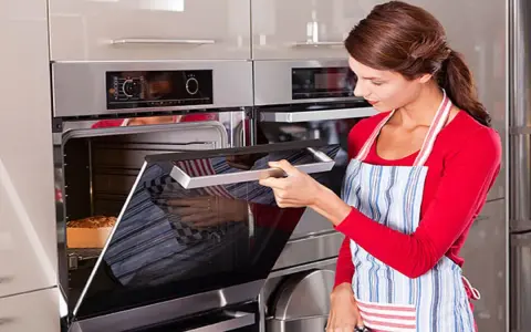 Mujer con delantal abre horno donde se hornea un pan.
