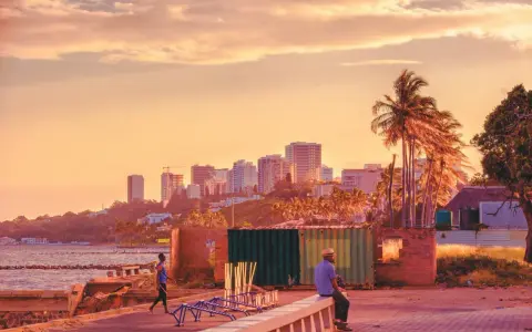 Zachód słońca nad Maputo, stolicą Mozambiku. W oddali widać panoramę miasta, a na pierwszym planie mężczyzna siedzi na murku.