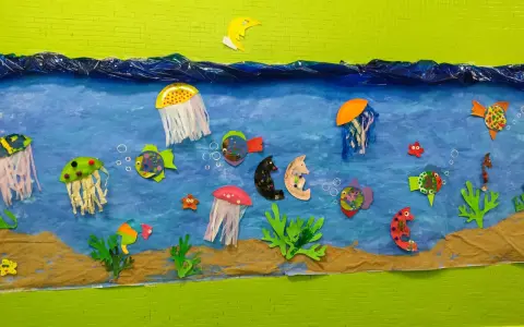 Un colorido mural de animales marinos infantiles con peces, medusas y caballitos de mar nadando en un mar azul, sobre arena.