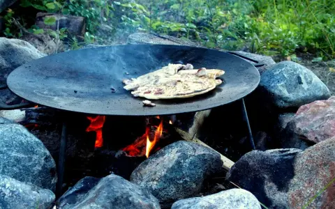 Matlagning över öppen eld på ett muurikka ställning. Pannkakor steks i en stor stekpanna över glödande kol och ved.