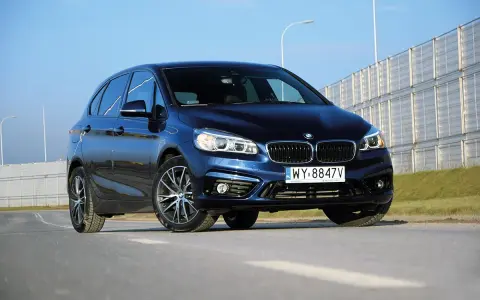 Ciemnoniebieski BMW van na tle jasnego nieba i barier dźwiękochłonnych.