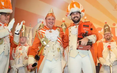 Narren in bunten Kostümen feiern jecke Tage. Ein Mann hält eine Kaffeemaschine, die anderen tragen prunkvolle Uniformen und Federhüte.