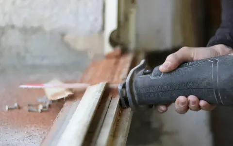 Main d'un artisan utilisant une scie sauteuse pour la dépose totale d'une fenêtre. Estimation du prix pose fenêtre dépose totale.