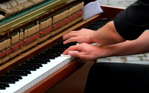 Mains sur le clavier d'un piano, prêt à jouer d'un instrument. Les marteaux et les cordes sont visibles.