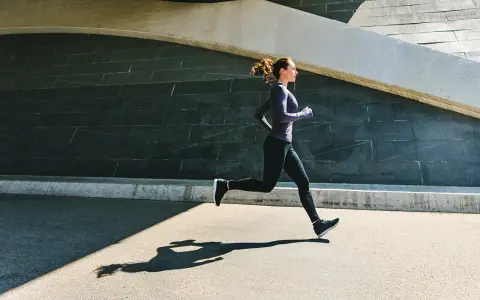 Frau im lila Oberteil und schwarzen Leggings beim aerobes Training, ihr Schatten auf dem Asphalt.