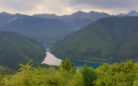 Valli boscose e un lago serpeggiante nella **Garfagnana e Lunigiana**, con montagne maestose sullo sfondo.