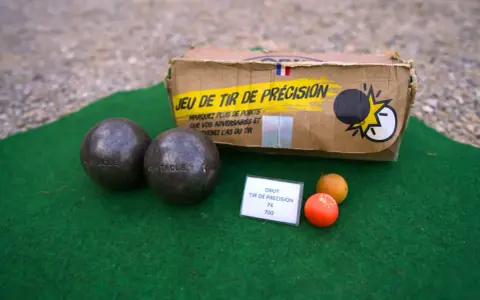 Deux boules de pétanque, un cochonnet et une boîte "Jeu de tir de précision" suggèrent un défi de poids et de diamètre pour le tireur.