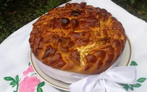Obrzędowe ciasto weselne, bogato zdobione, z plecionkami i kwiatami z ciasta, na haftowanym obrusie.