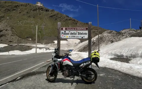 Moto pronta per affrontare il Passo dello Stelvio, con neve ai lati della strada e un edificio in cima alla montagna.