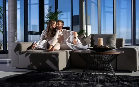 Pareja disfrutando de un momento íntimo en un sofá moderno, ideal para alquileres de temporada con vistas panorámicas.