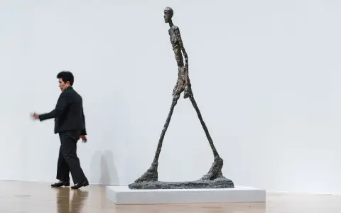 Un homme qui marche, une sculpture élancée, semble se déplacer dans un espace blanc.