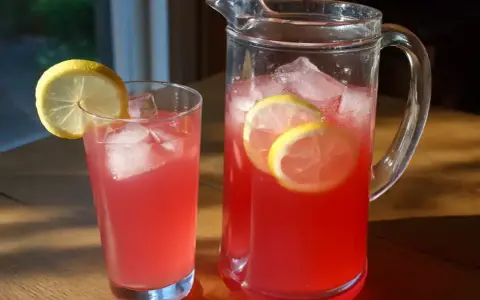 En karaff och ett glas med rosa rabarbersaft, is och citronskivor. Perfekt för ett enkelt rabarbersaft recept.